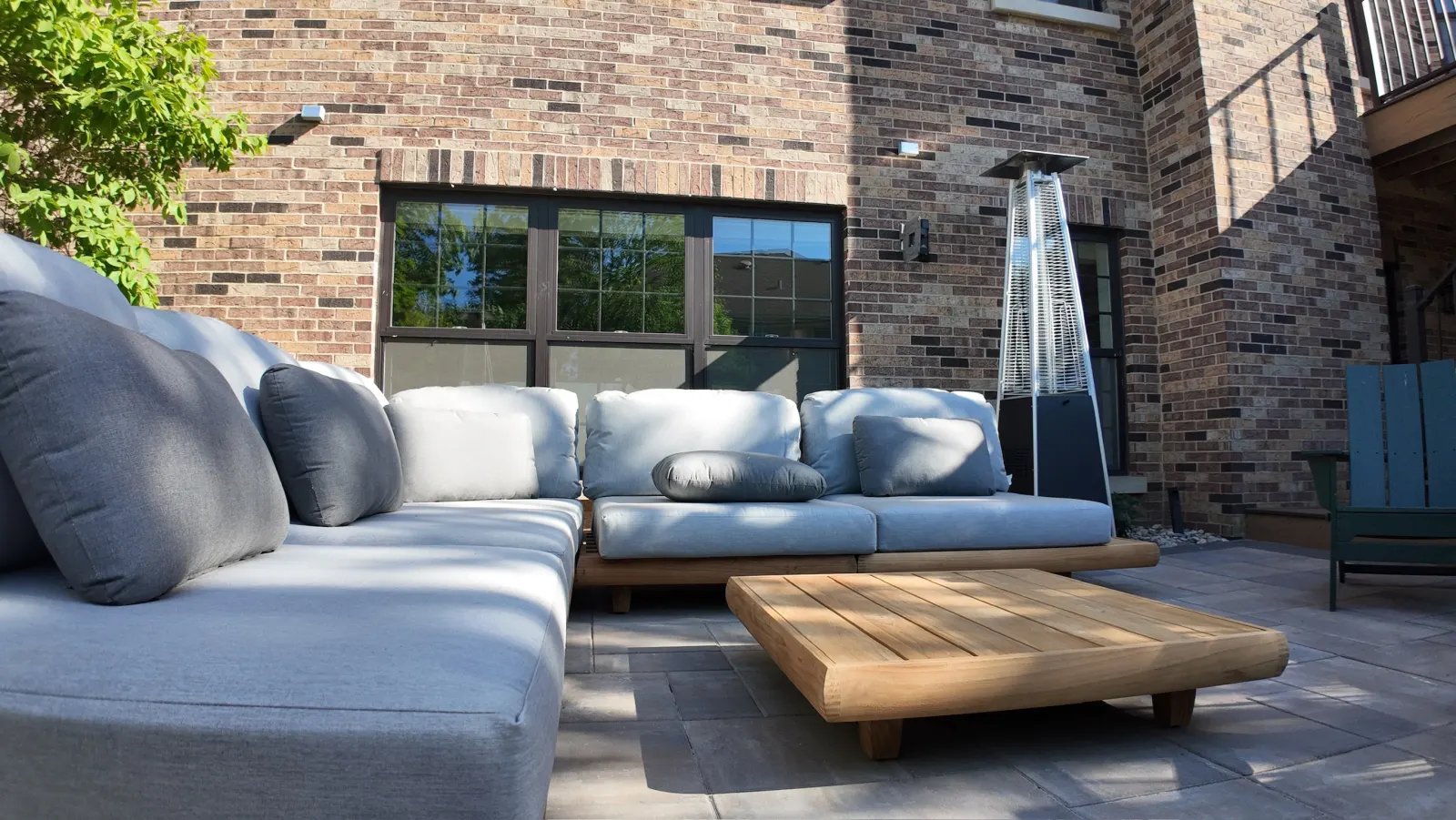 Luxury outdoor living paver patio with teak sectional sofa against brick home